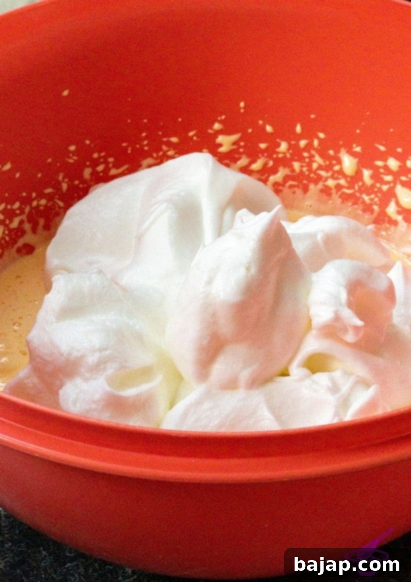 The process of gently folding stiffly beaten egg whites into a foamy egg yolk and sugar mixture, showing the light, airy texture of the combined batter.
