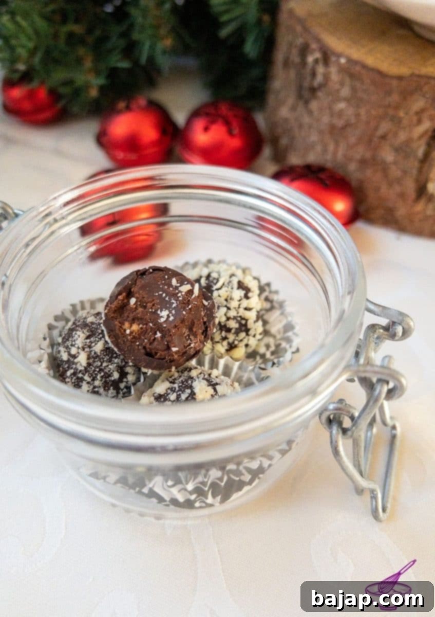 Orange Marmalade Truffles with Dark Chocolate rolled in minced almonds on white tablecloth. Christmas decoration in the back.