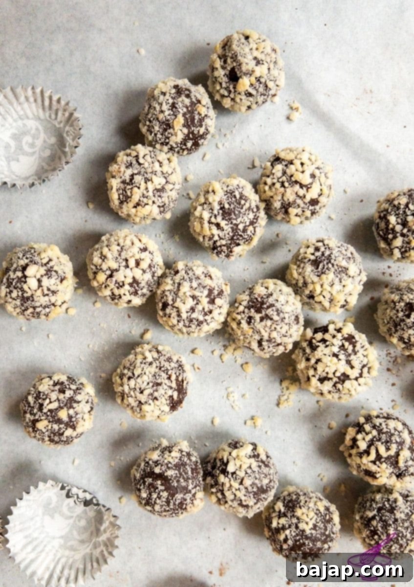 Orange Marmalade Truffles with Dark Chocolate rolled in minced almonds on white tablecloth. Christmas decoration in the back.