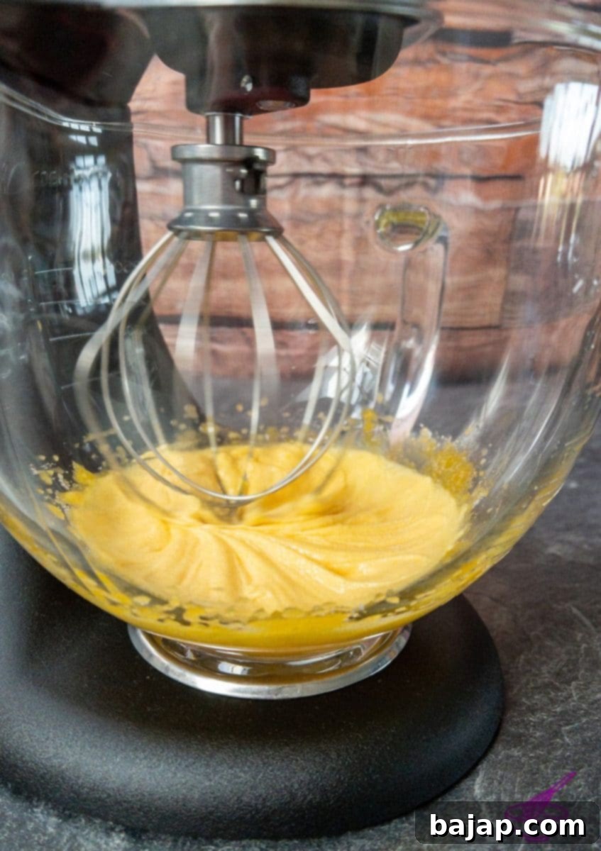 Egg yolks and granulated sugar being whisked in a KitchenAid mixer until pale and thick, forming the custard base.