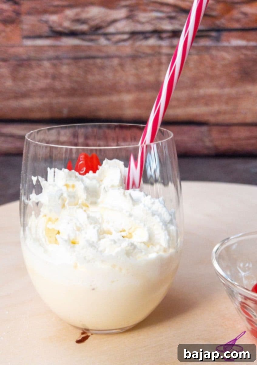 Spiked Eggnog Milkshake 4 A freshly made boozy eggnog milkshake, garnished with whipped cream and a cherry, ready to drink with a straw.