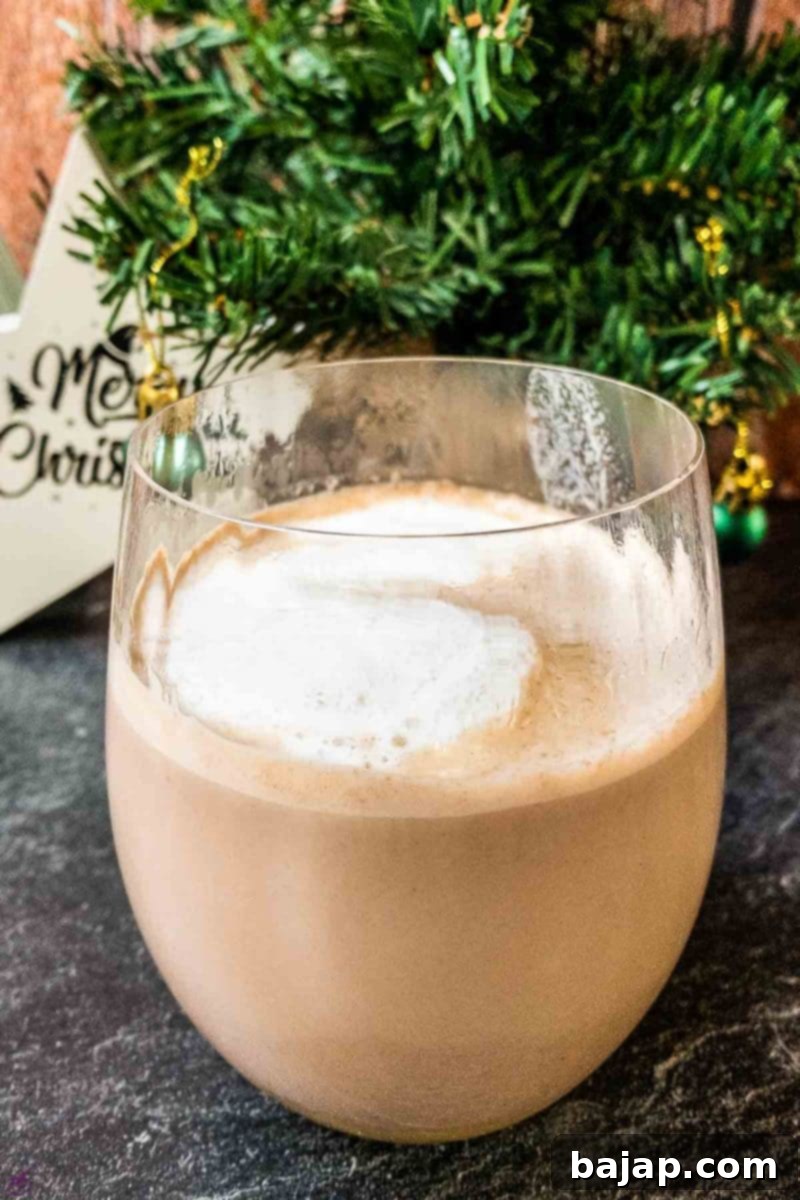 A festive glass of eggnog hot chocolate topped with creamy foam, ready to be enjoyed.