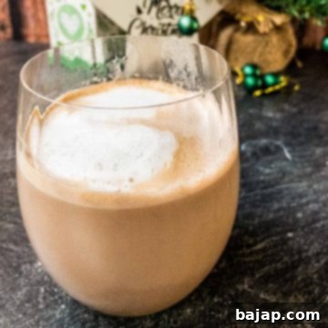 Delicious Eggnog Hot Chocolate in a glass with fluffy milk foam and chocolate shavings.