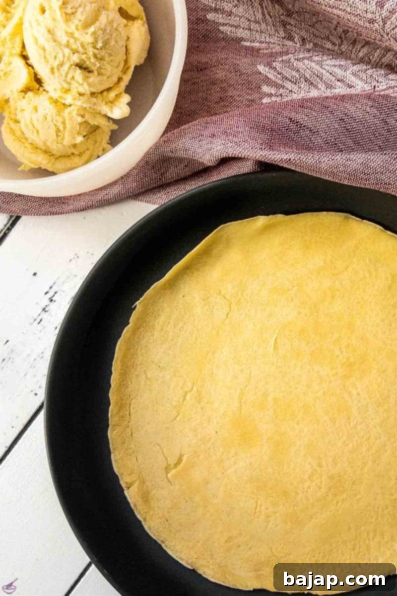 A single warm, thin pancake laid flat on a white plate, ready for filling.