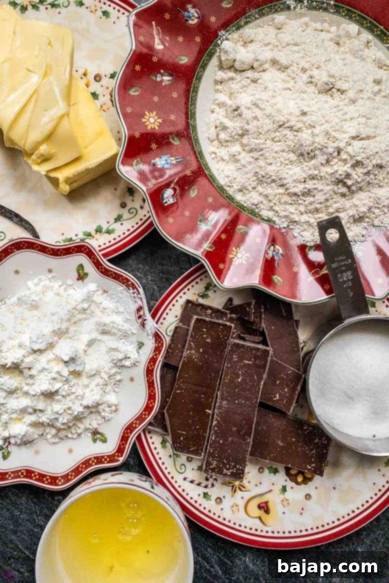 A flat lay image of all the essential ingredients for making chocolate dipped butter cookies: unsalted butter, sugar, vanilla bean, egg whites, cake flour, cornstarch, and dark chocolate couverture.