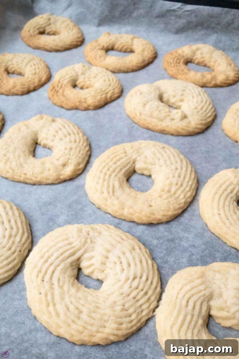 Freshly baked butter cookies on a cooling rack, showing their pale golden color and distinct piped shapes.