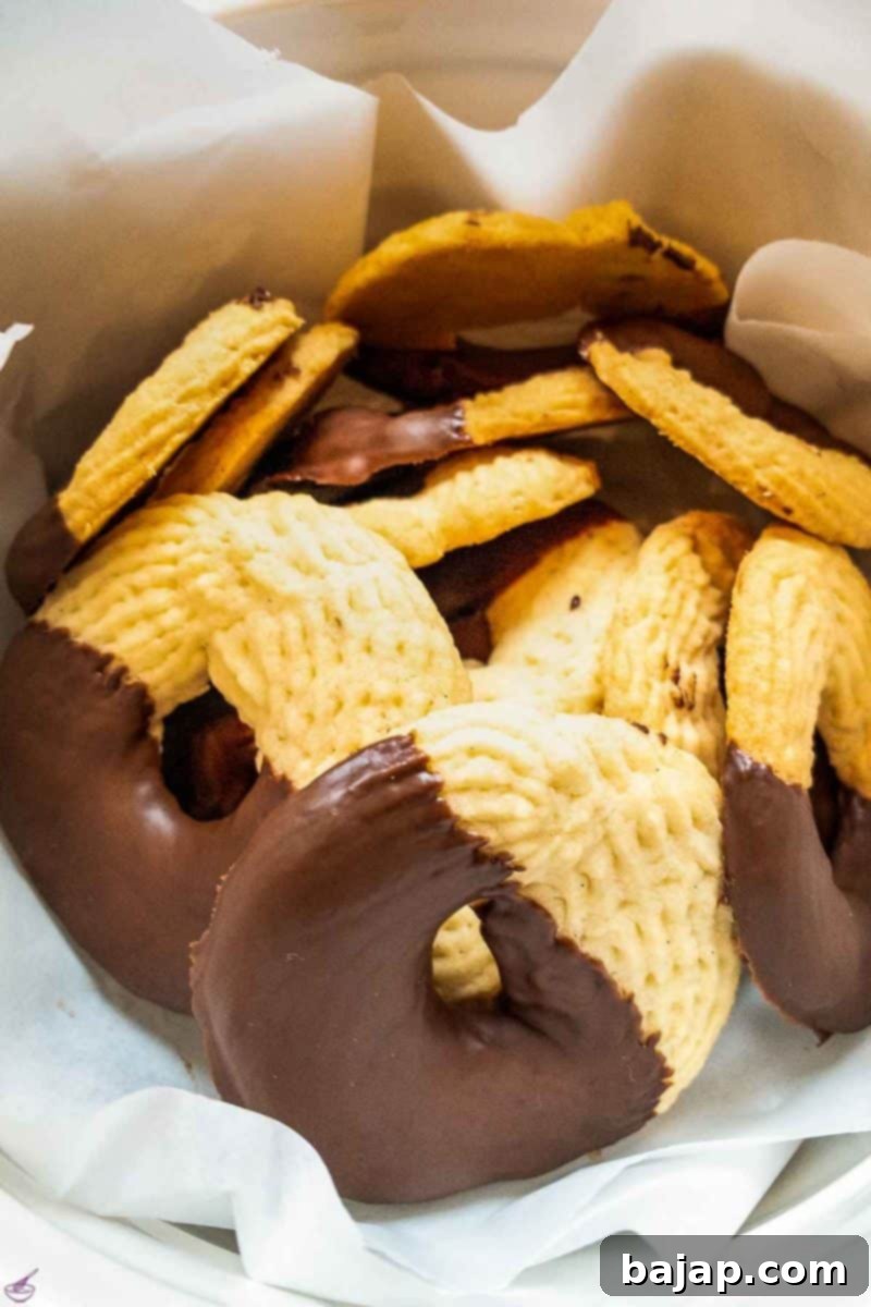 Ready-to-eat chocolate-dipped butter cookies neatly arranged in a cookie jar, lined with parchment paper.