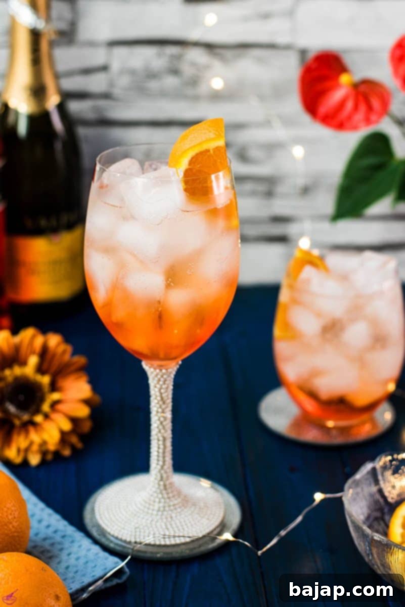 Wonderful layered Aperol Spritz cocktail, tart and delicious, garnished with an orange slice. Placed on a mirror coaster on a blue wooden background.