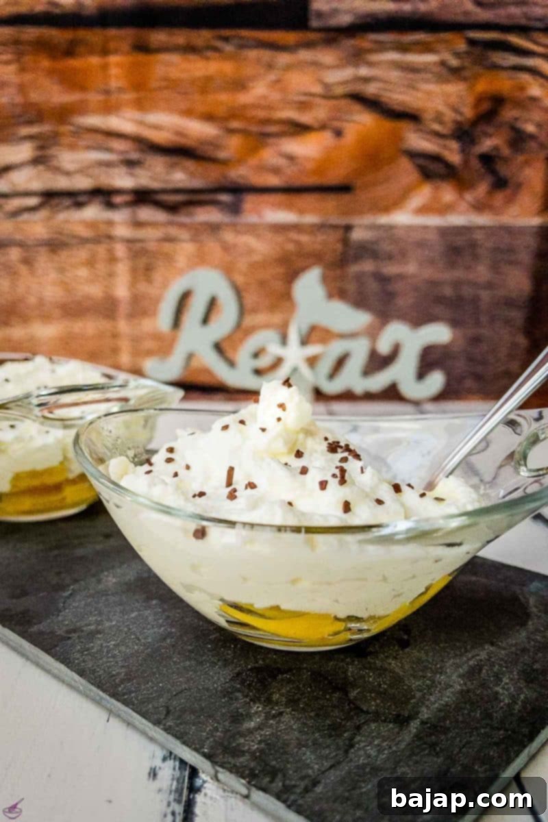 Glass serving bowl with pineapple, whipped cream, and chocolate sprinkles on black stone plate. A perfect easy no-bake dessert for summer.