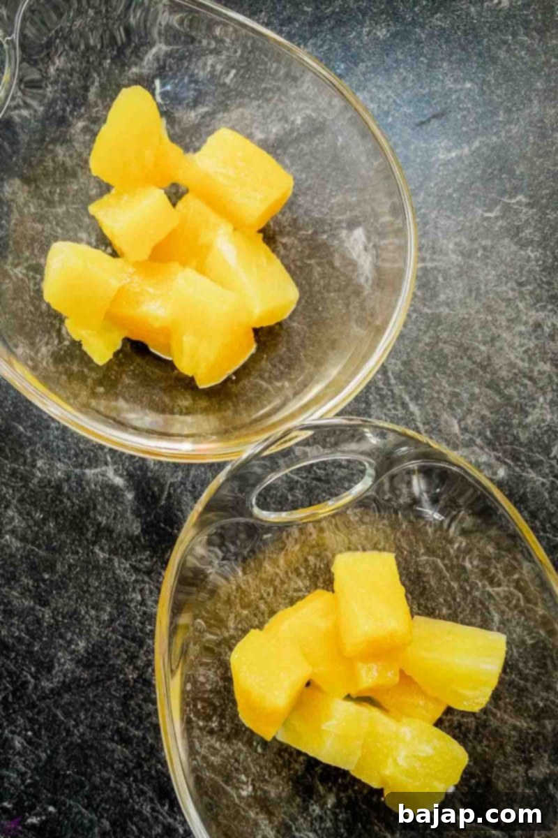 Overhead shot of two glass serving bowls filled with pineapple chunks, forming the first layer of the dessert.