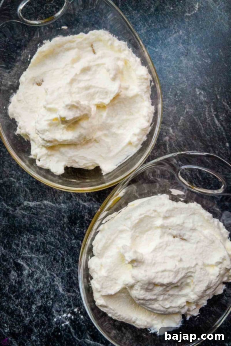 Overhead shot of two glass serving bowls filled with pineapple chunks and a generous layer of whipped cream on top, forming the second layer.