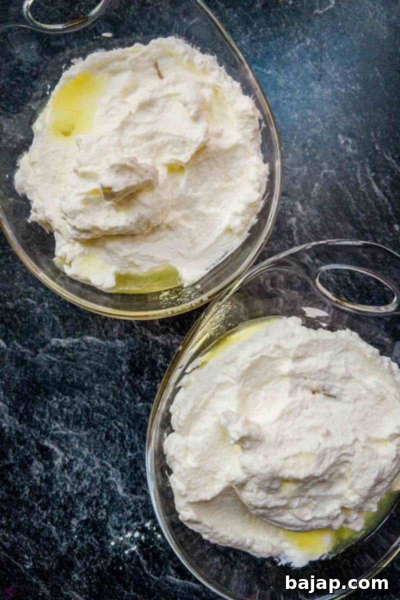 Overhead shot of two glass serving bowls with pineapple chunks and whipped cream, now with a drizzle of strained pineapple juice.