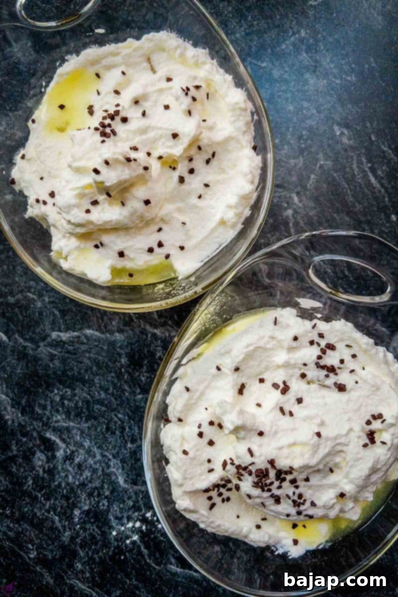 Overhead shot of two glass serving bowls filled with pineapple chunks, whipped cream and chocolate sprinkles.