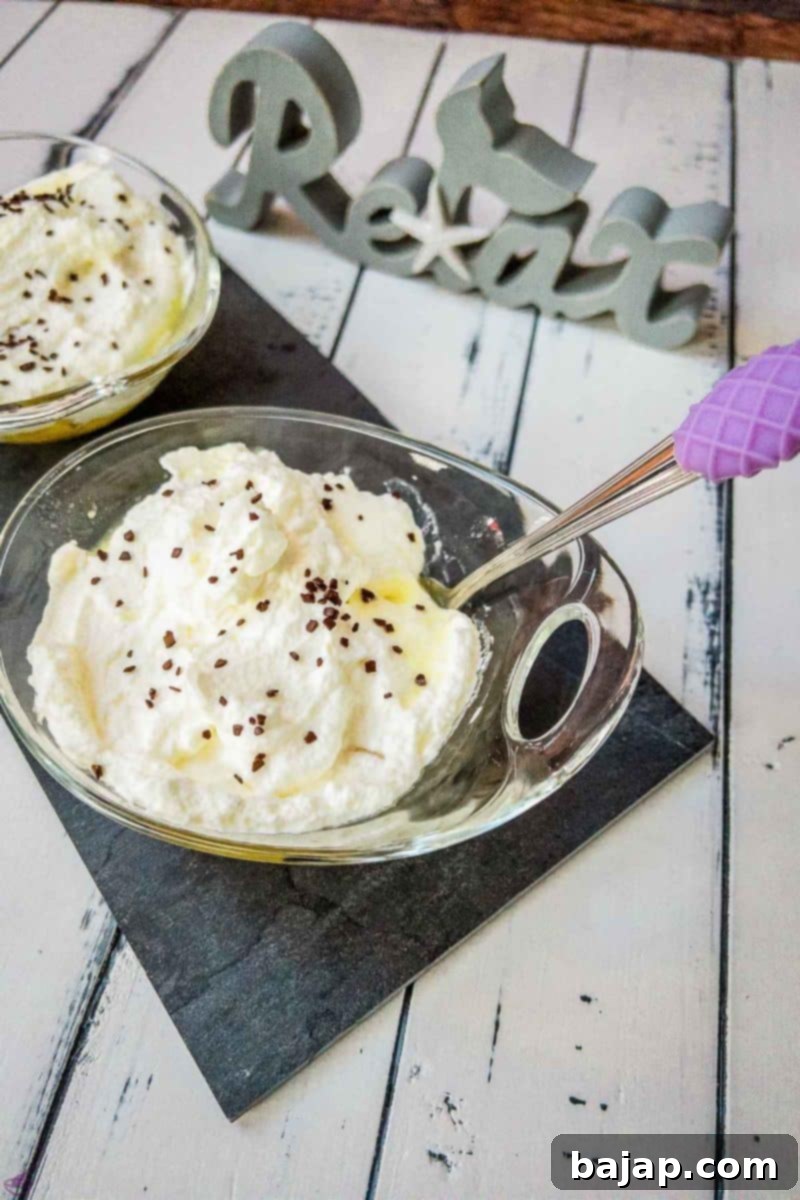 Glass serving bowl with pineapple, whipped cream, and chocolate sprinkles on black stone plate, showcasing the dessert's elegant presentation.