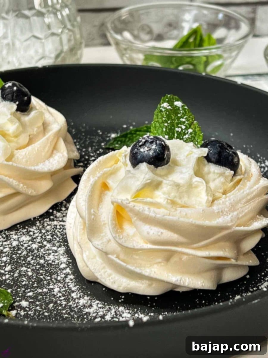 Berry Burst Pavlova Clouds 2 Meringue nests filled with whipped cream, decorated with fresh blueberries and mint leaves, and lightly dusted with powdered sugar. Presented on an elegant black serving plate, highlighting the vibrant colors and delicate textures.