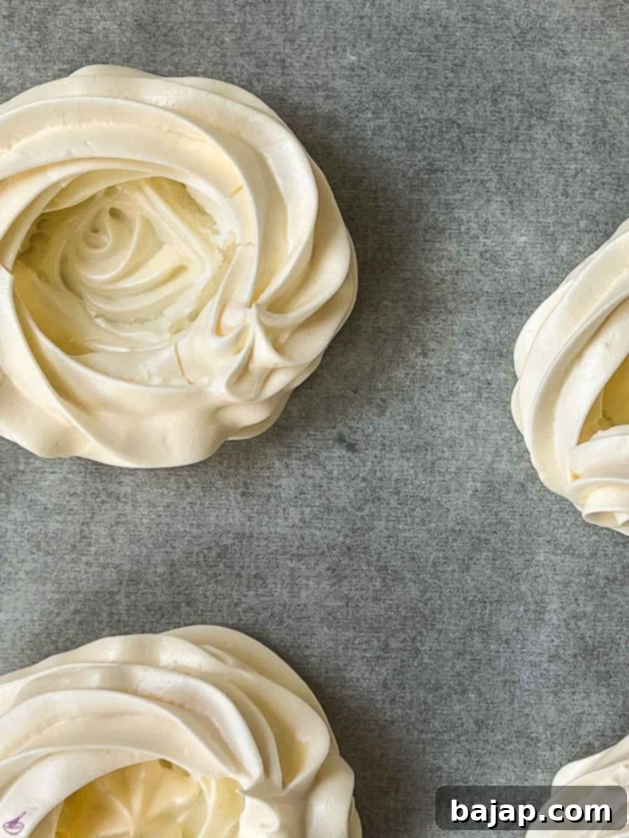 Berry Burst Pavlova Clouds 5 Perfectly baked meringue nests, lightly golden and crisp, cooling on a baking tray after being removed from the oven. Their shape is well-preserved, indicating successful baking and a delicate, airy texture.
