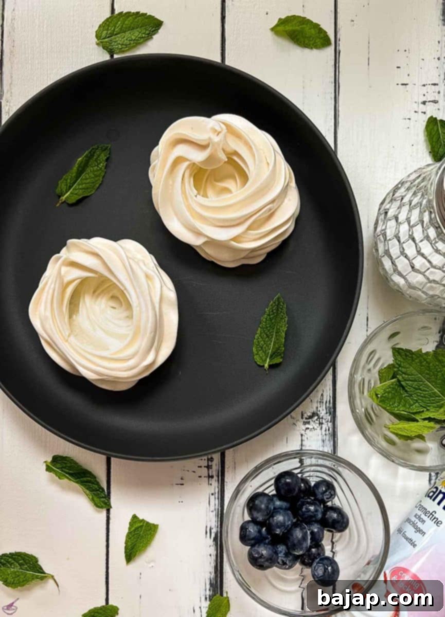 Berry Burst Pavlova Clouds 6 A crisp meringue nest delicately placed on a black serving plate, showcasing its pristine white color and delicate texture, ready to be filled and garnished for a perfect dessert.