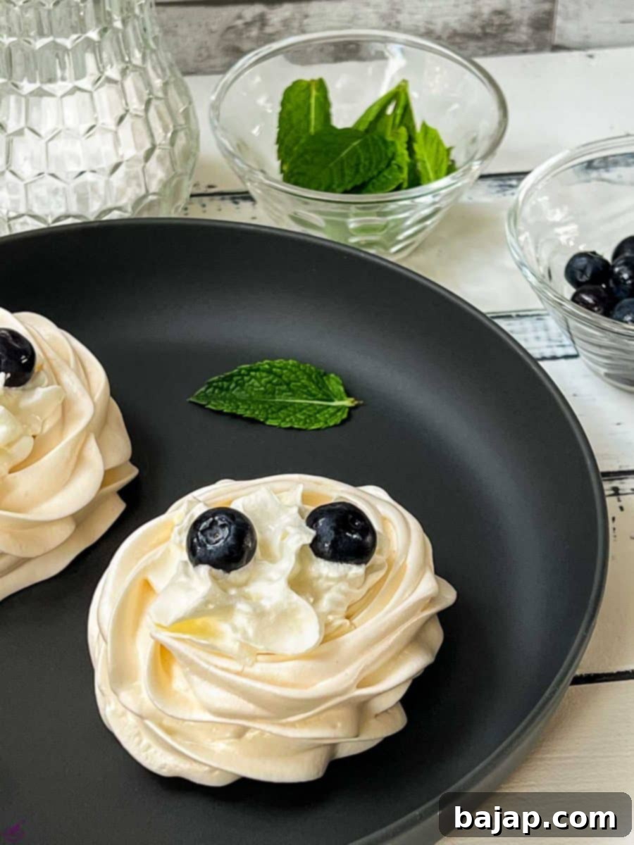 Berry Burst Pavlova Clouds 8 A meringue nest on a black serving plate, filled with whipped cream and abundantly garnished with vibrant blueberries, creating a rich visual contrast and inviting texture.