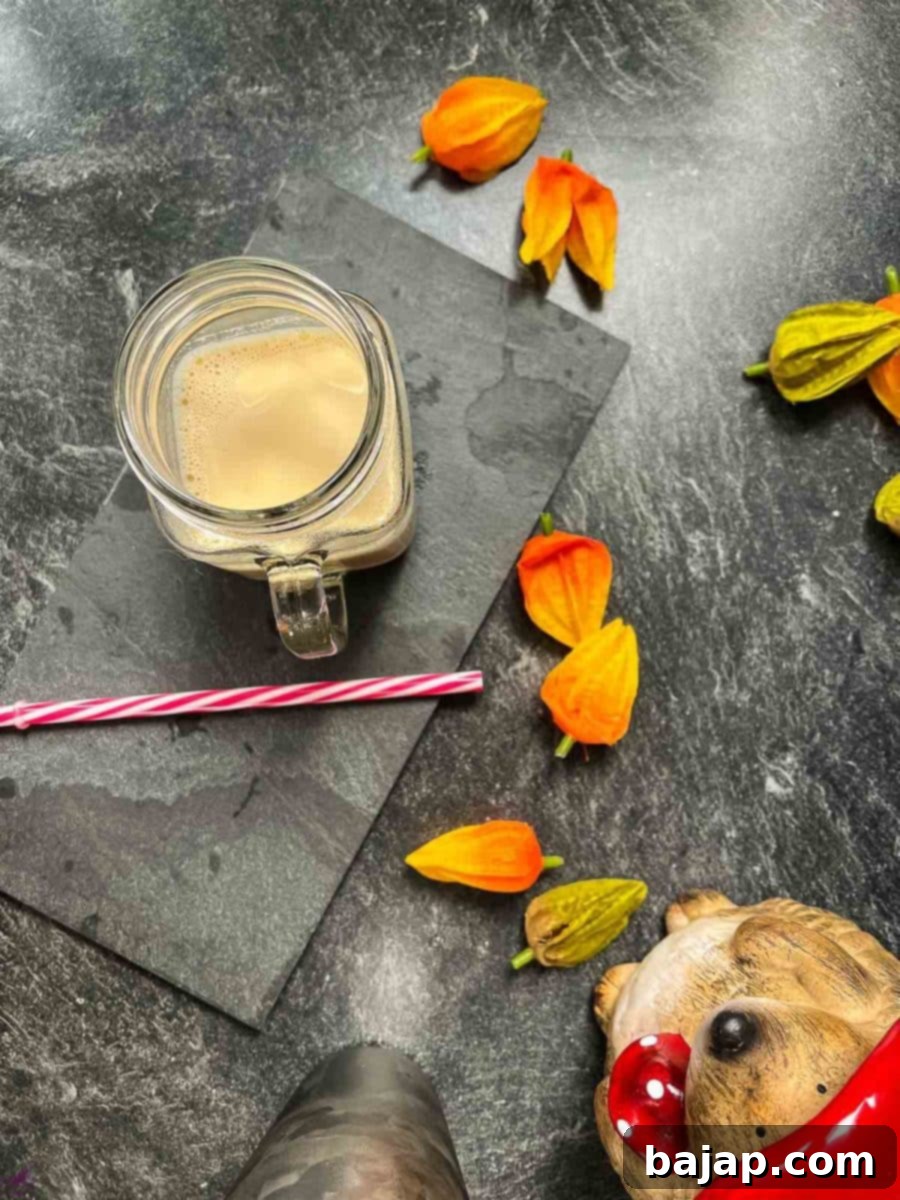 Easy 2 Ingredient Caramel Milk 8 Overhead shot - caramel milk in glass on dark plate with red and white plastic straw alongeside.