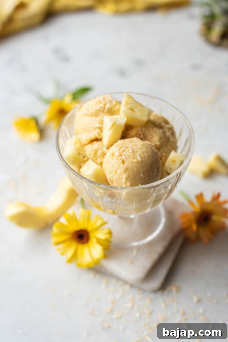 A scoop of coconut pineapple ice cream with fresh pineapple chunks.