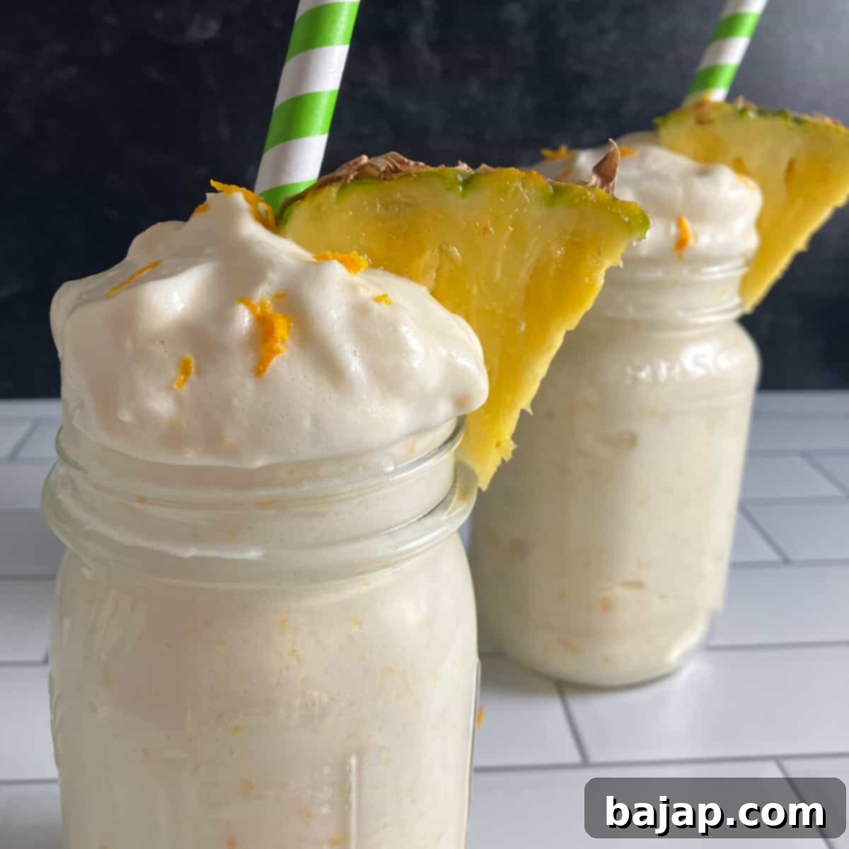 Two glasses of refreshing peach pineapple smoothie, garnished with fresh fruit.