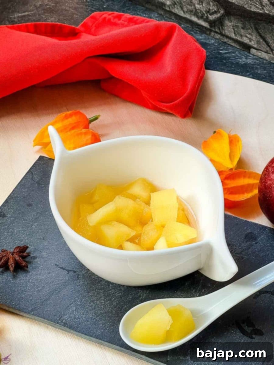 White ceramic bowl with apple compote. Decorated with apples and orange flowers placed on the side. 