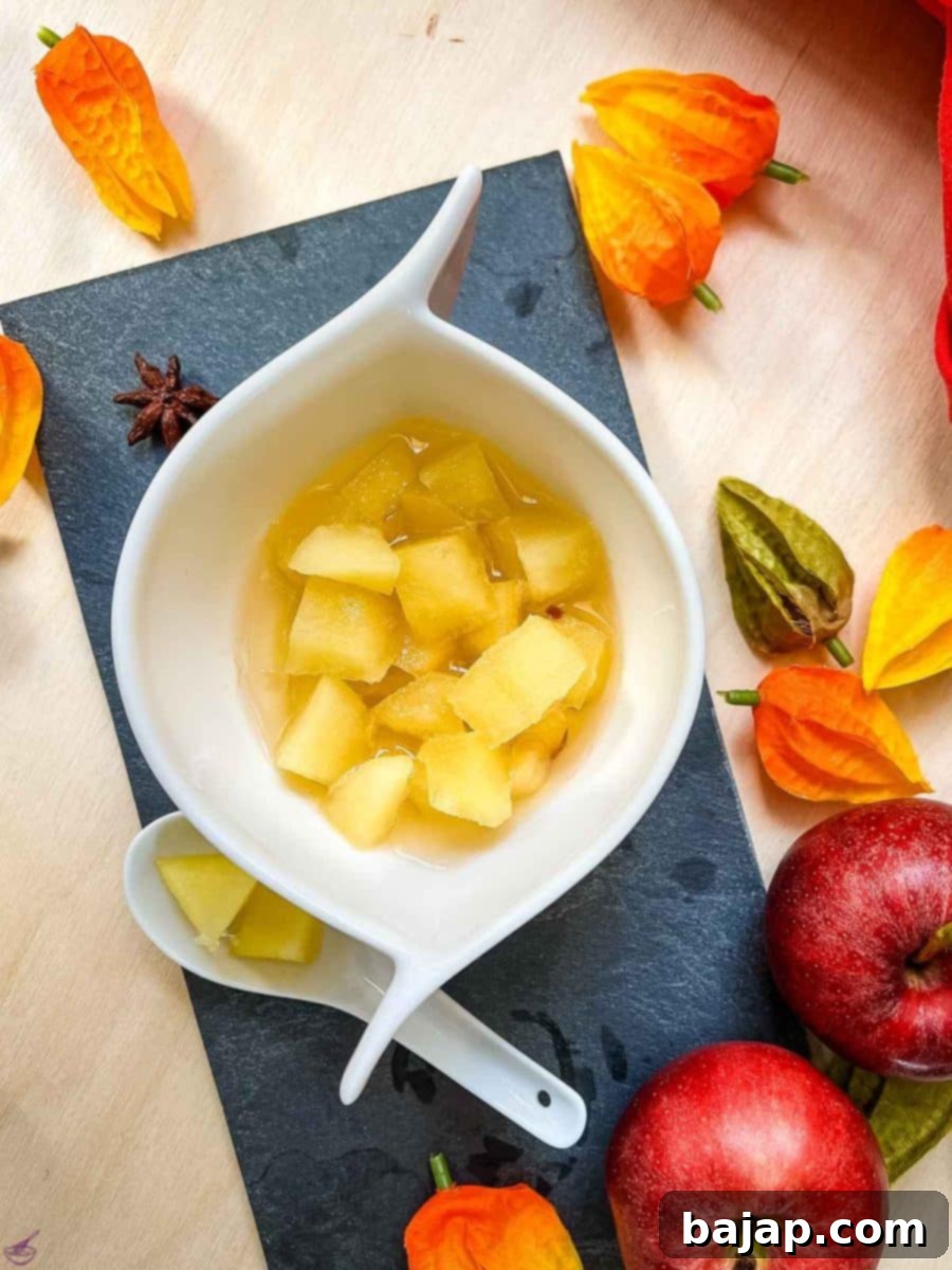 Easy Homemade Apple Compote 8 White ceramic bowl with apple compote. Decorated with apples, and orange flowers placed on the side.