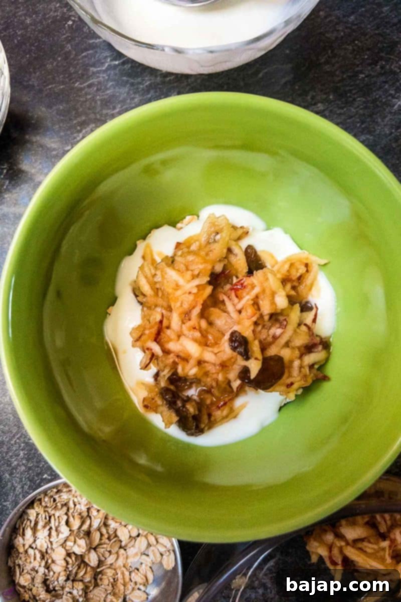 Bowl filled with a layer of oatmeal, yogurt and grated apples. 