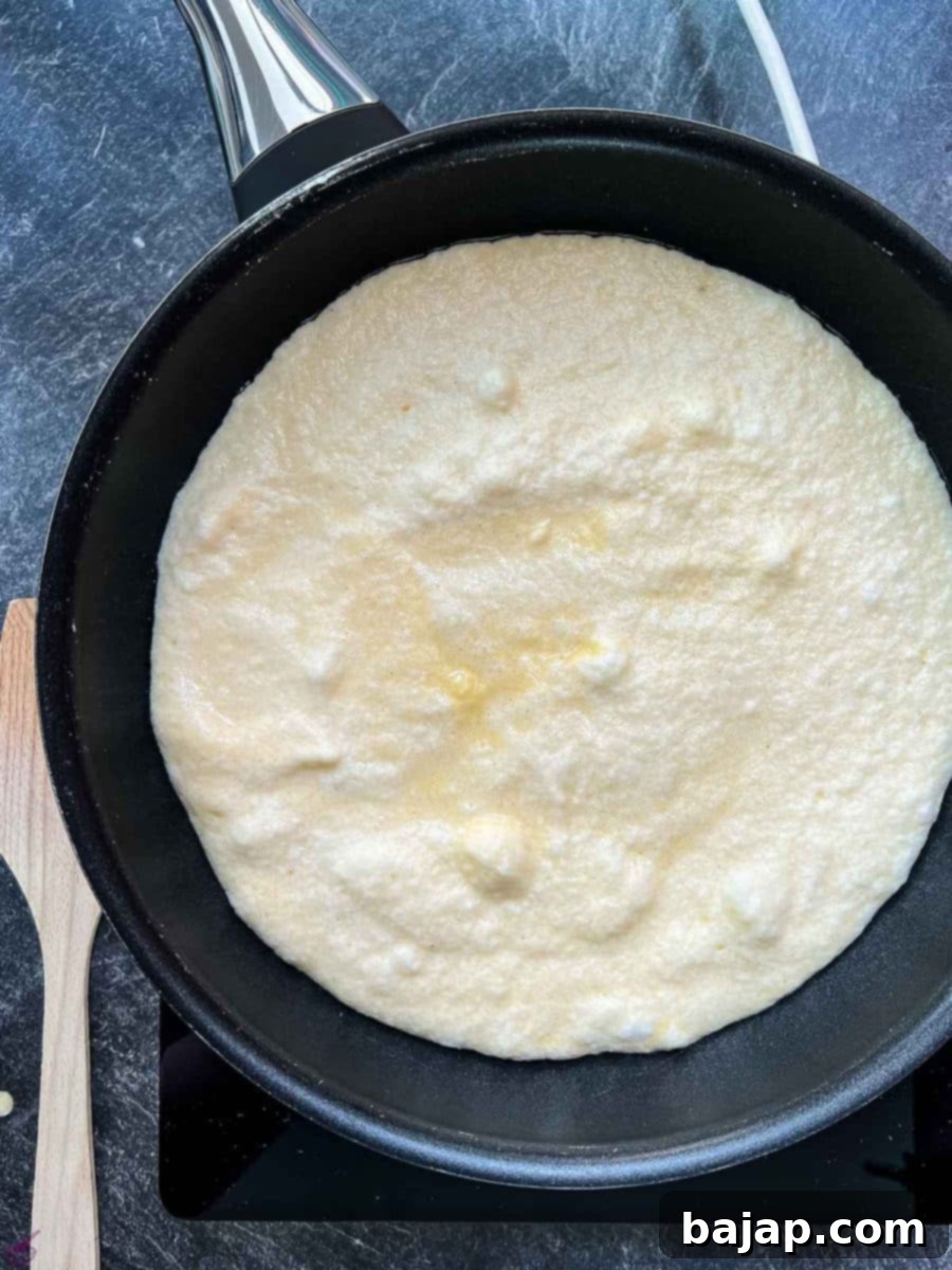 Thick pancake batter frying in a hot non-stick pan, turning golden brown on the bottom.