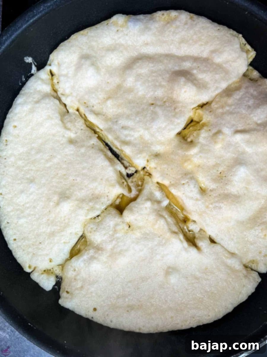 A large, golden-brown pancake being divided into four quarters directly in the frying pan using two spatulas.