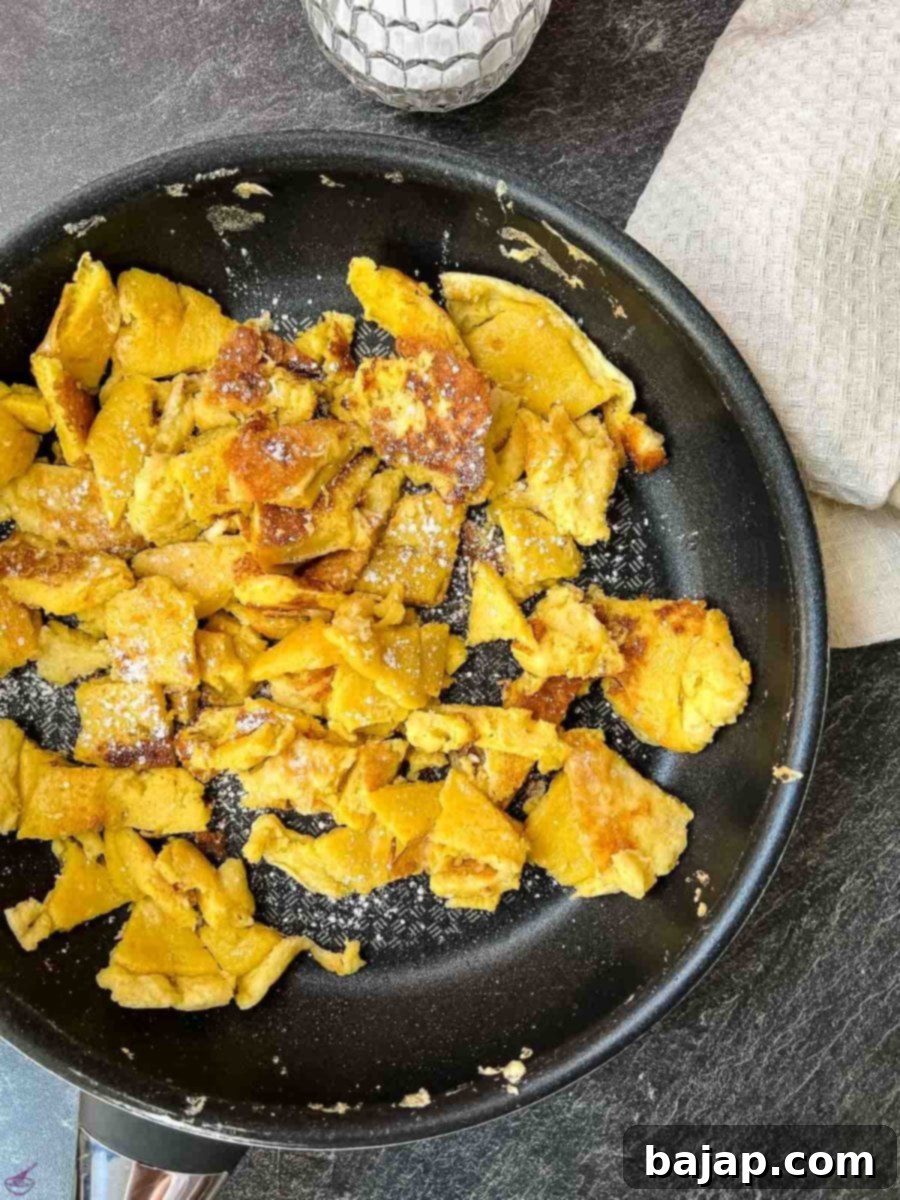 Kaiserschmarrn being torn into bite-sized pieces directly in the frying pan using two spatulas.