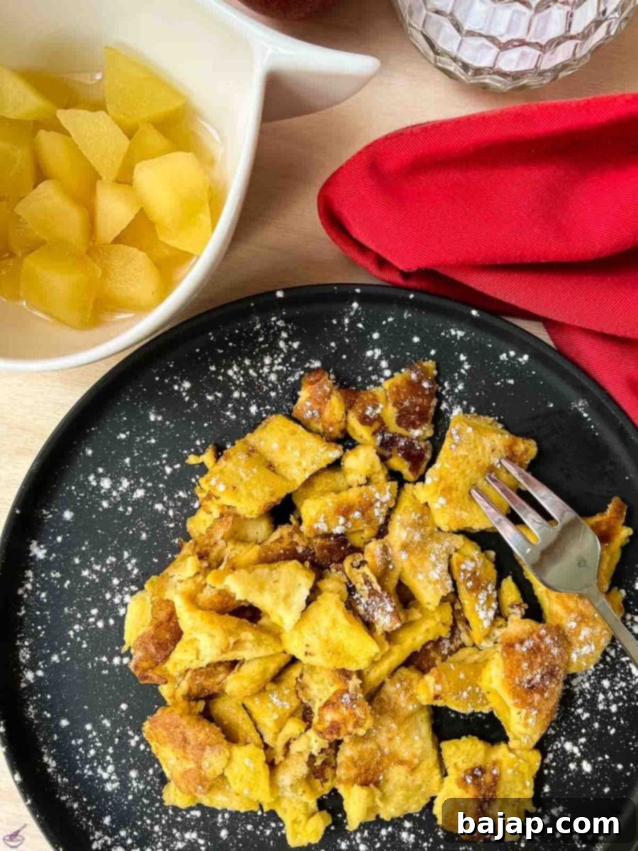 A serving of finished Kaiserschmarrn with powdered sugar and apple compote, garnished with fresh mint.