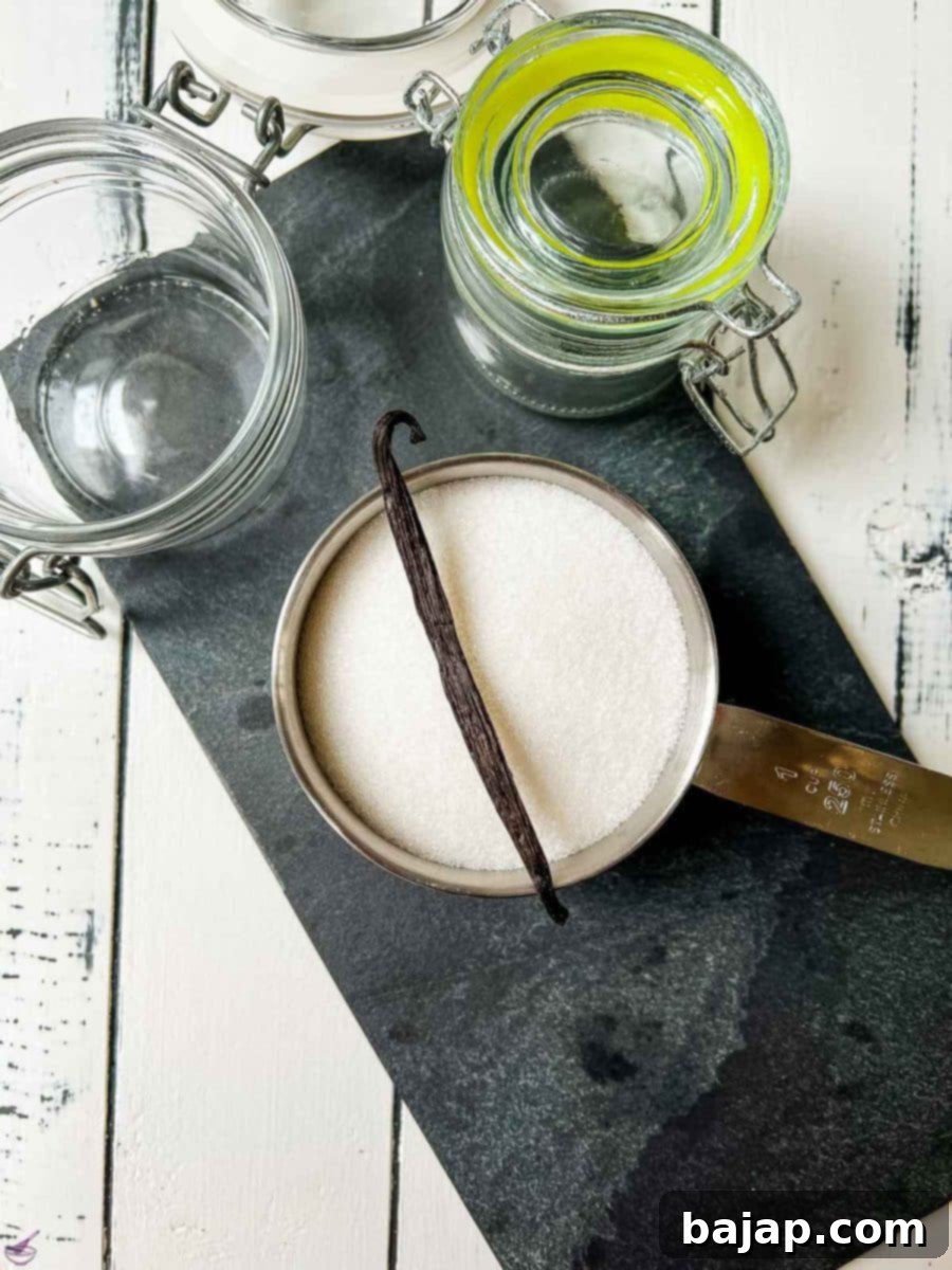 A single fragrant vanilla bean resting elegantly on a mound of bright white granulated sugar on a black stone board.