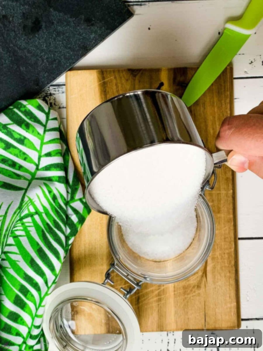 A close-up of a scraped vanilla bean being placed into a preserving jar already partially filled with sugar.