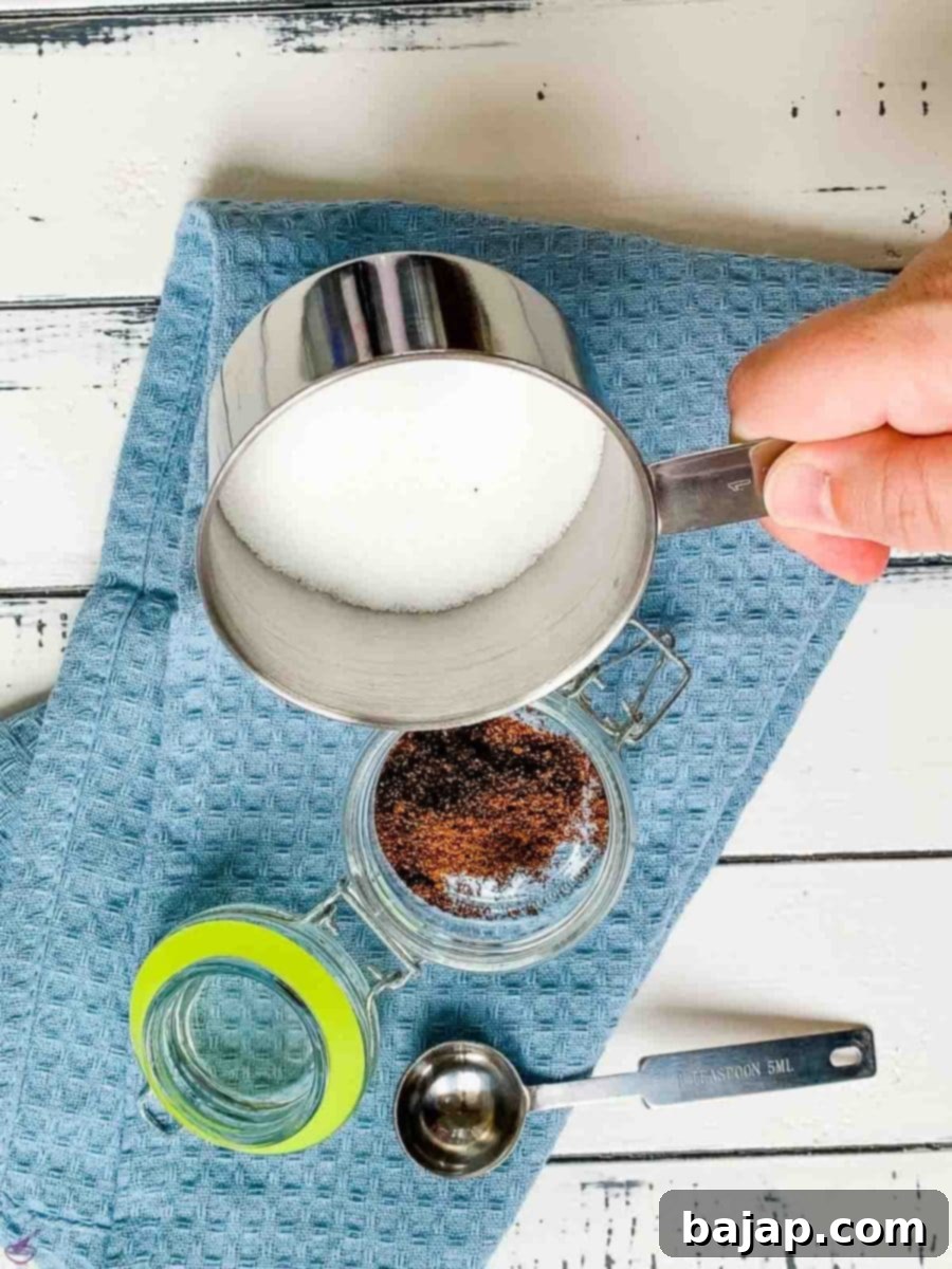 A close-up of granulated sugar being poured into a jar, covering the ground vanilla powder at the bottom.