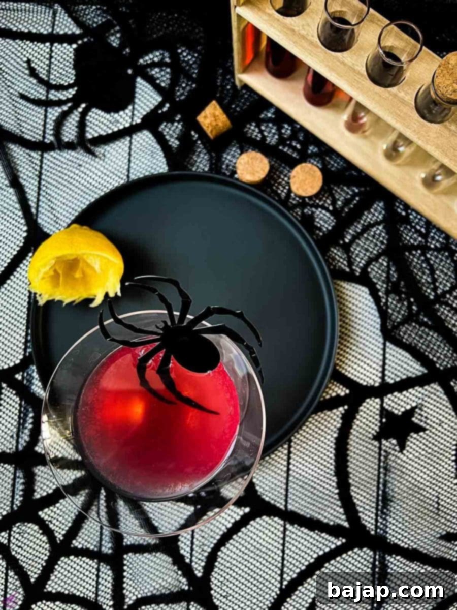 Blood red Halloween cocktail in glass decorated with spider. Black serving plate and spider web decoration.