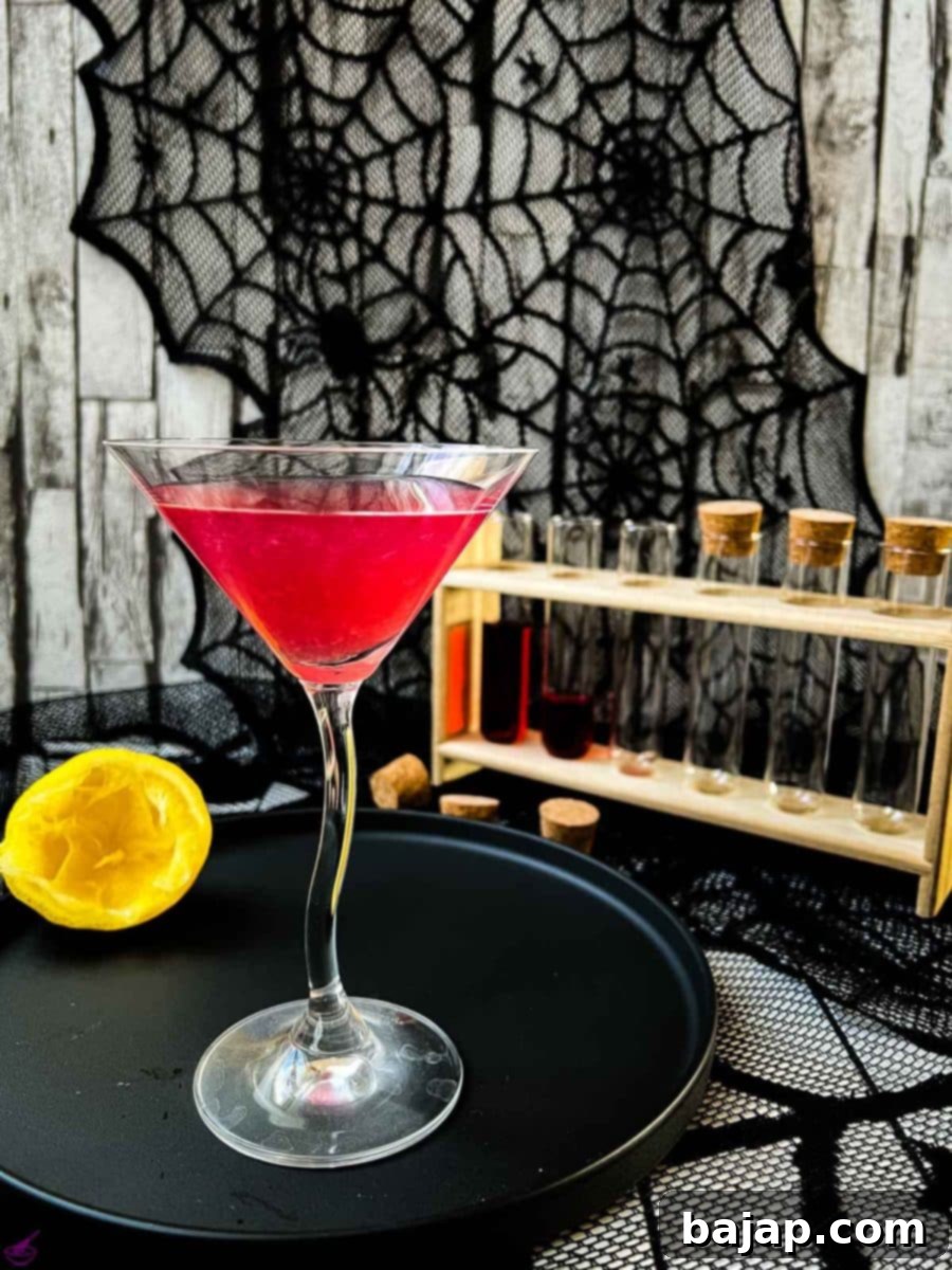 Blood red Halloween cocktail in glass decorated with spider. Black serving plate and spider web decoration.