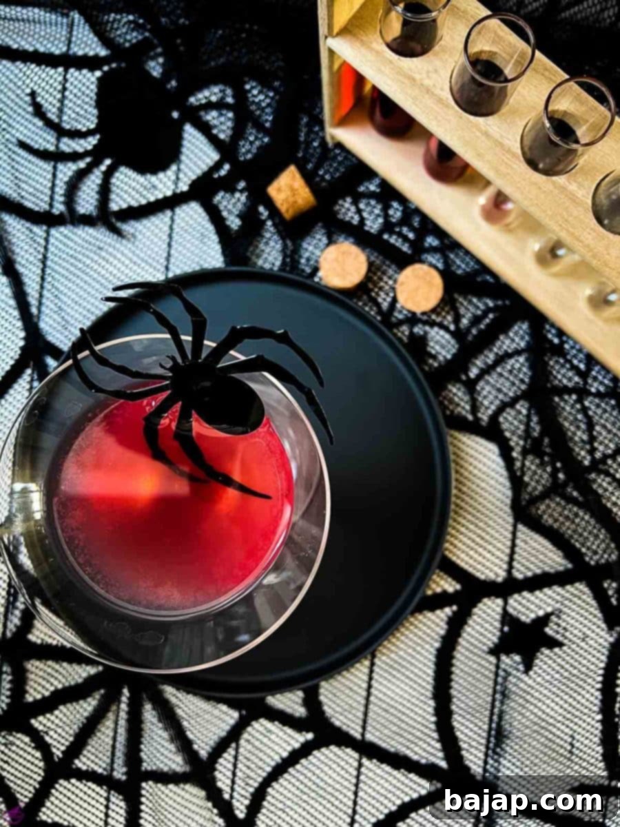 Blood red Halloween cocktail in glass decorated with spider. Black serving plate and spider web decoration.