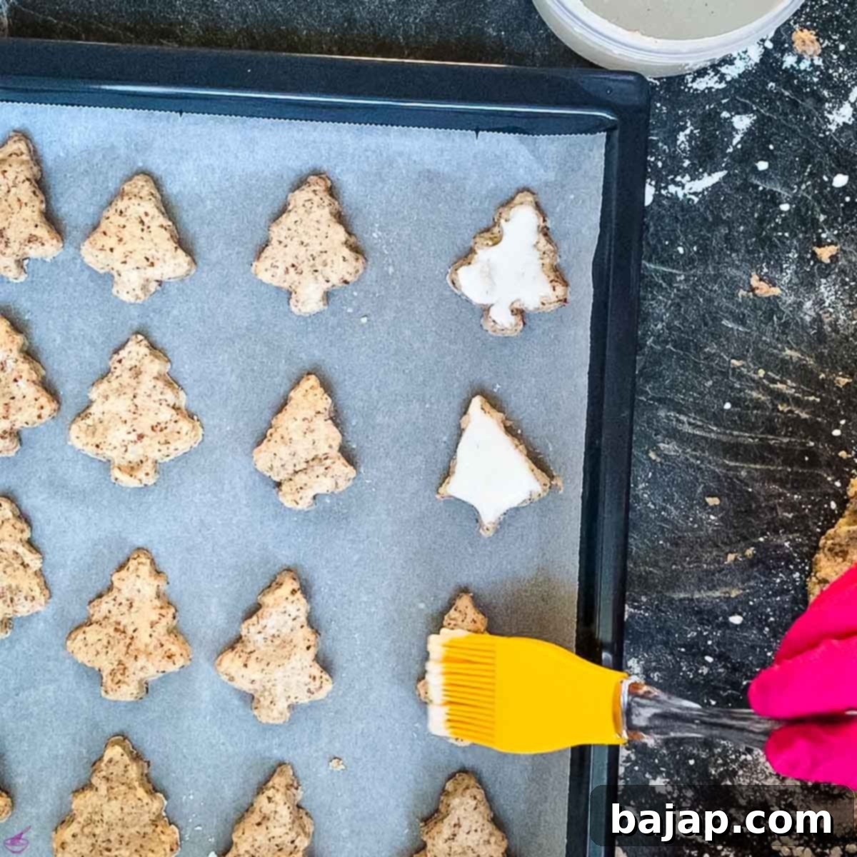 Brushing the cut-out cinnamon tree cookies with a sugar and egg white glaze before baking.