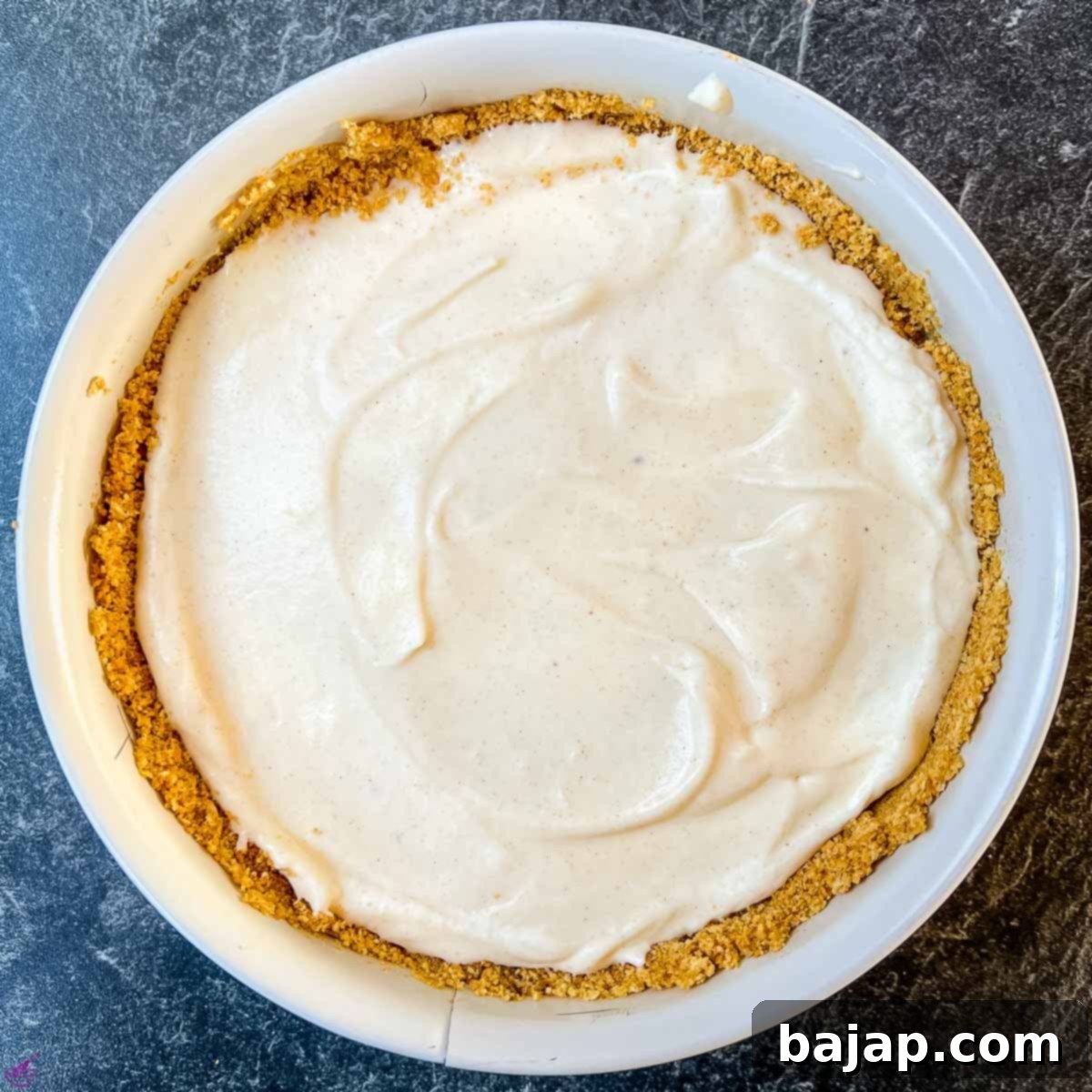 Filling the prepared graham cracker crust with the creamy eggnog cheesecake mixture before chilling.