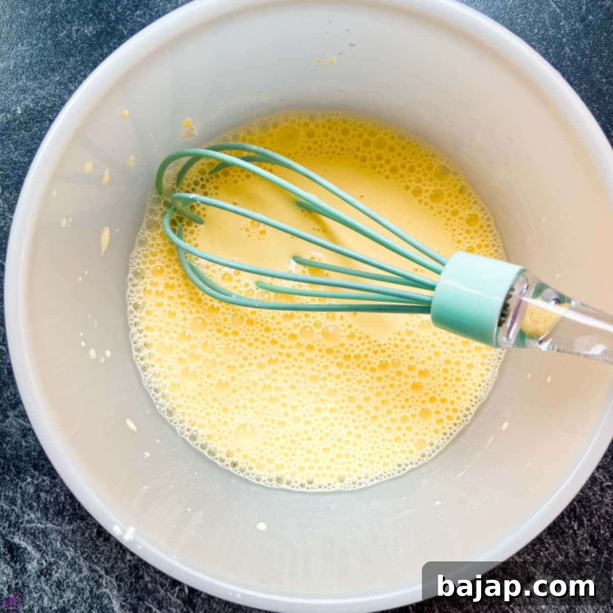 Whisking cold milk with vanilla pudding powder in a mixing bowl until completely smooth.