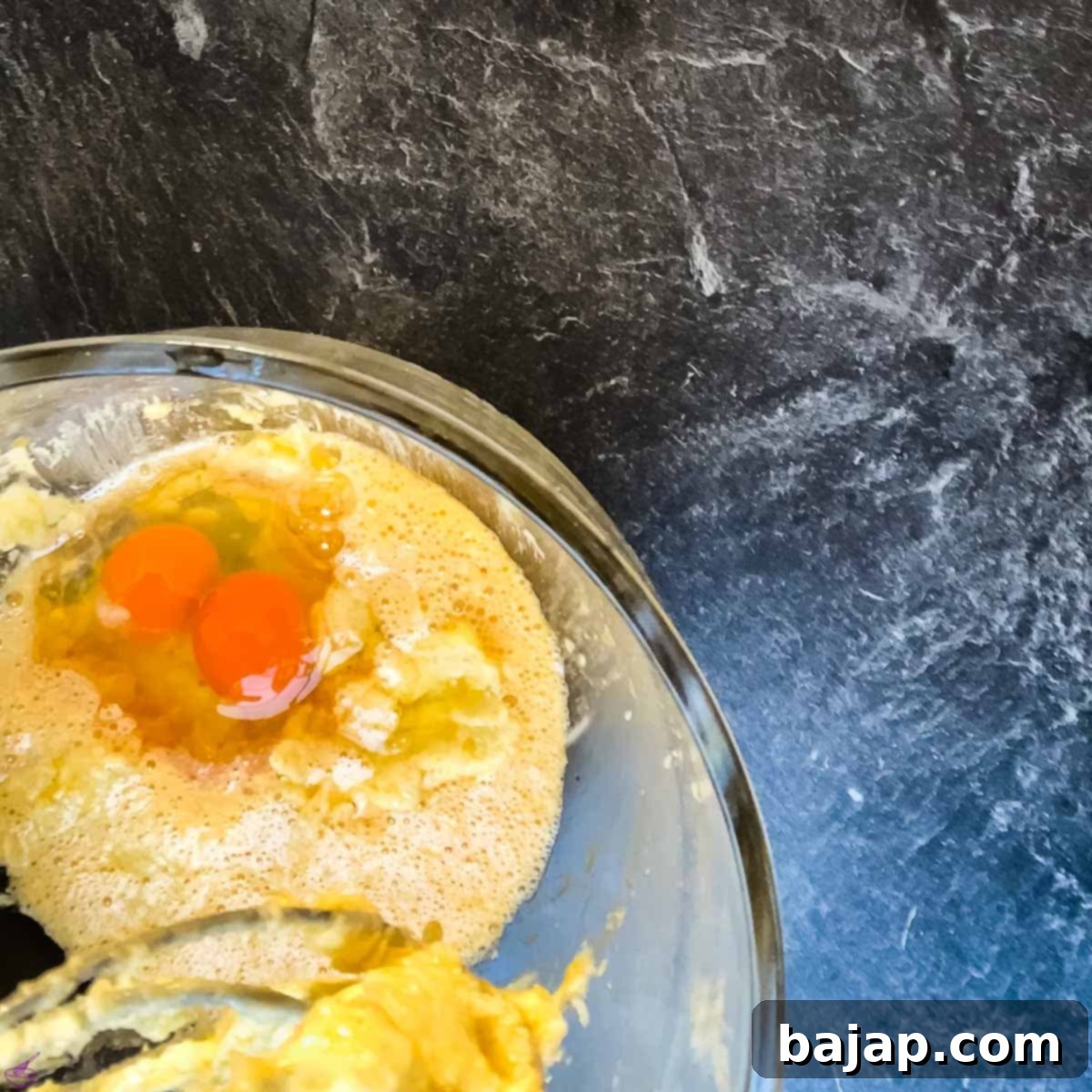 Adding room-temperature eggs one by one to the creamed butter and sugar mixture.