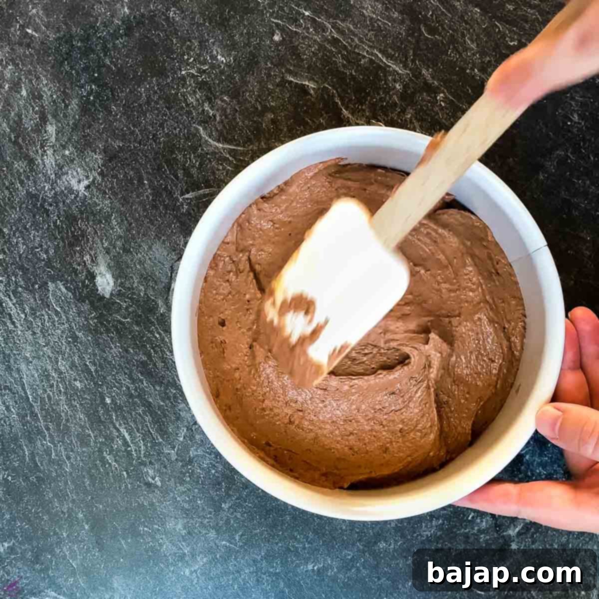 A springform pan evenly filled with thick, dark chocolate cake batter.
