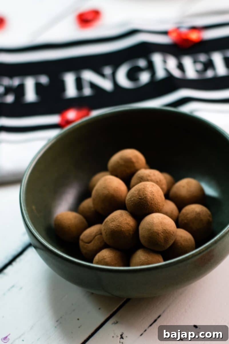 Delicious marzipan potatoes in a dark green bowl on white wooden ground, showcasing their cocoa dusting and perfect round shape.