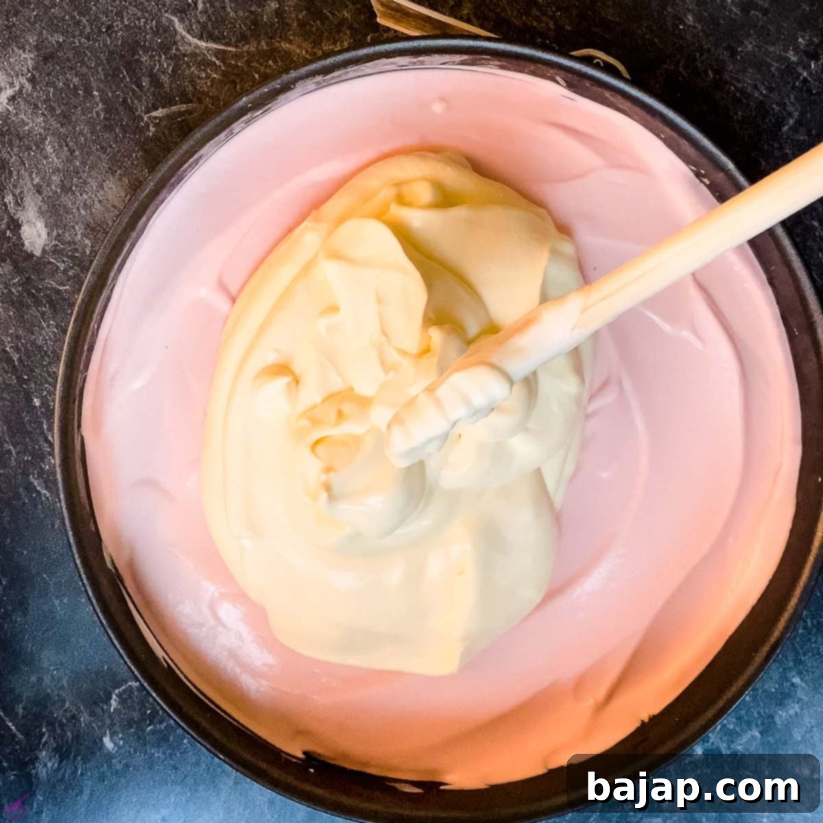 Finishing the cheesecake with the smooth orange cream cheese layer spread on top of the raspberry layer.