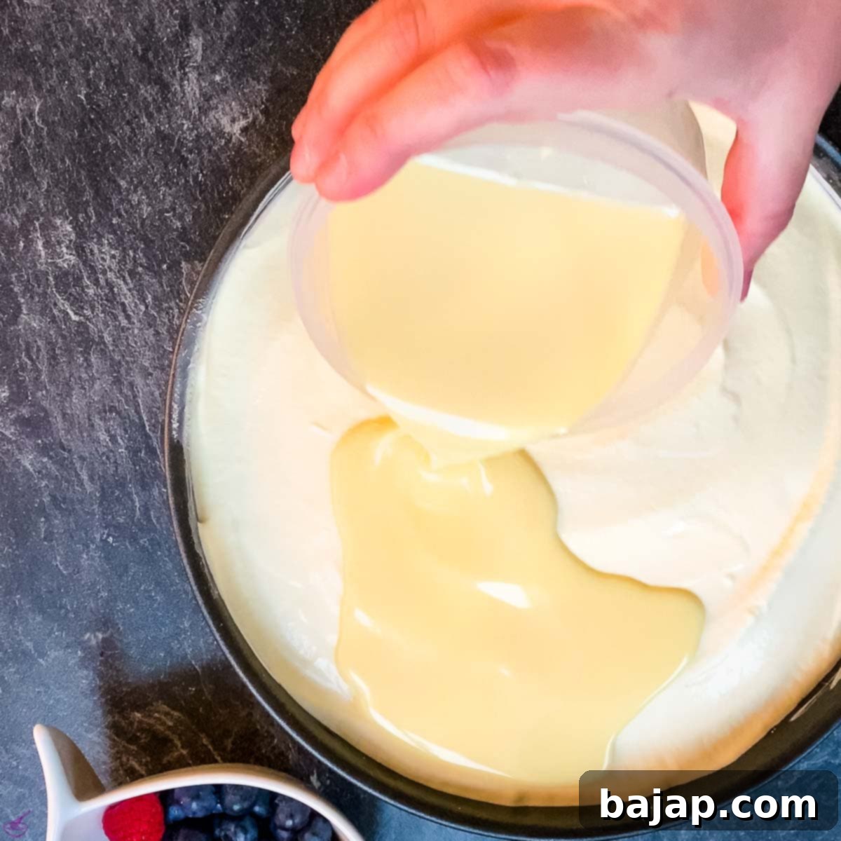 Pouring the freshly prepared glossy white chocolate glaze over the chilled orange cheesecake layer, creating a smooth finish.