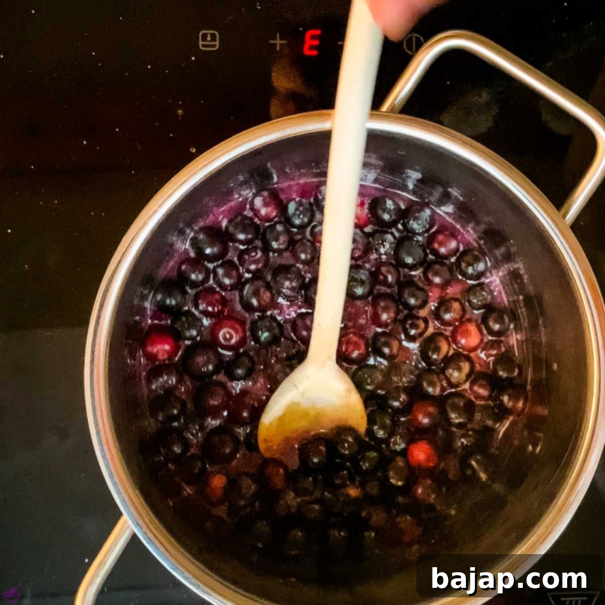 Preparing the blueberry sauce on the stove, stirring fresh blueberries with sugar and water to create a vibrant flavoring for the cheesecake layer.