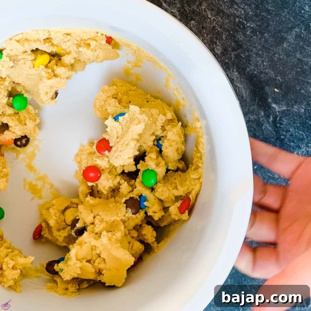 Close-up of vibrant cookie dough with colorful M&Ms perfectly mixed in, ready for scooping.
