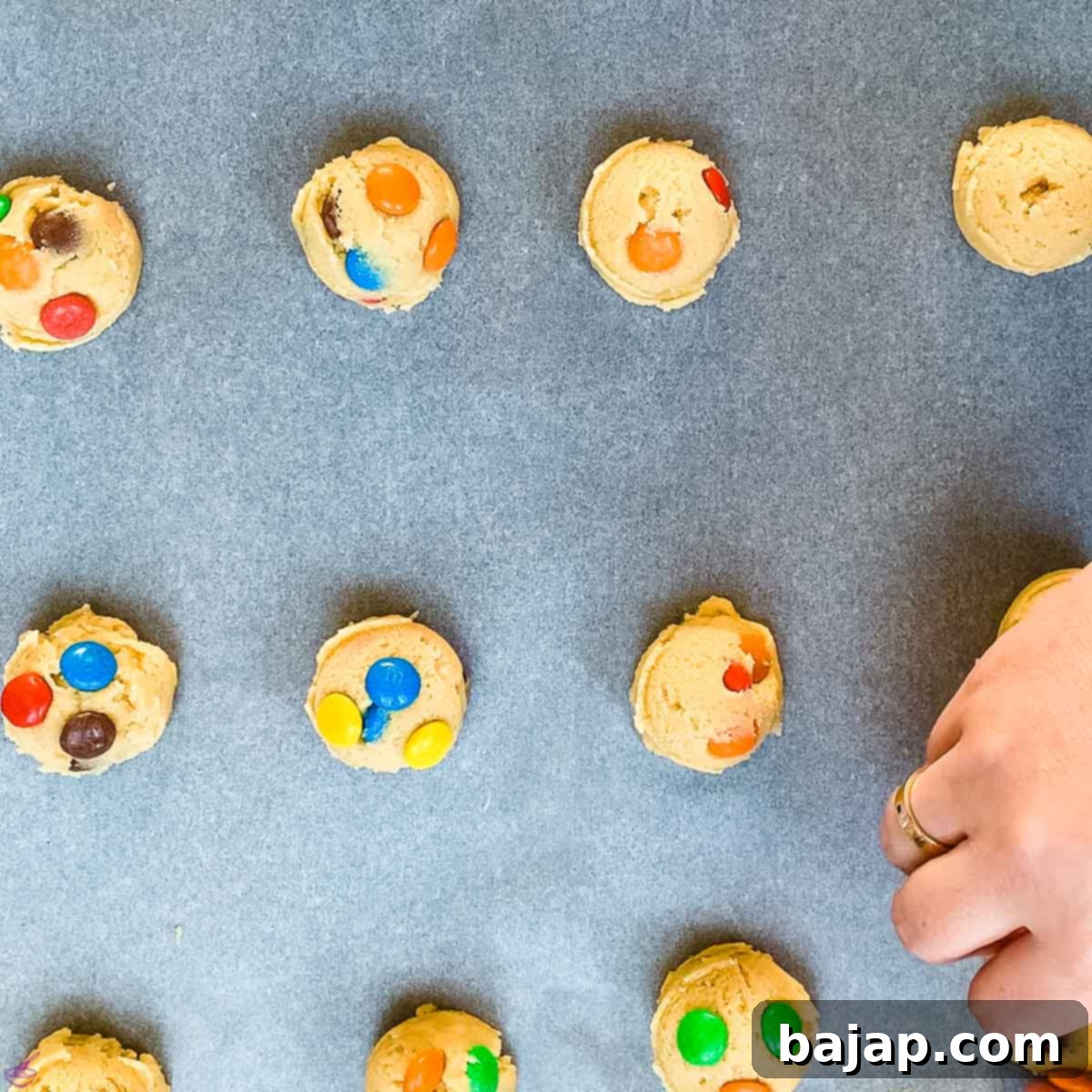 Remaining M&Ms being pressed into the tops of cookie dough balls for a vibrant finish.