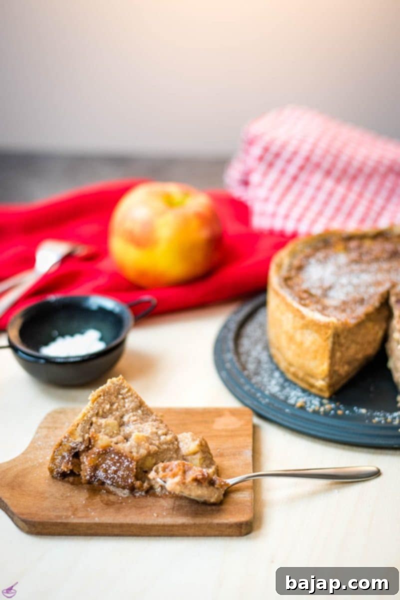 Delicious slice of a luscious apple tart, placed on a wooden cutting board, with a spoon beside.